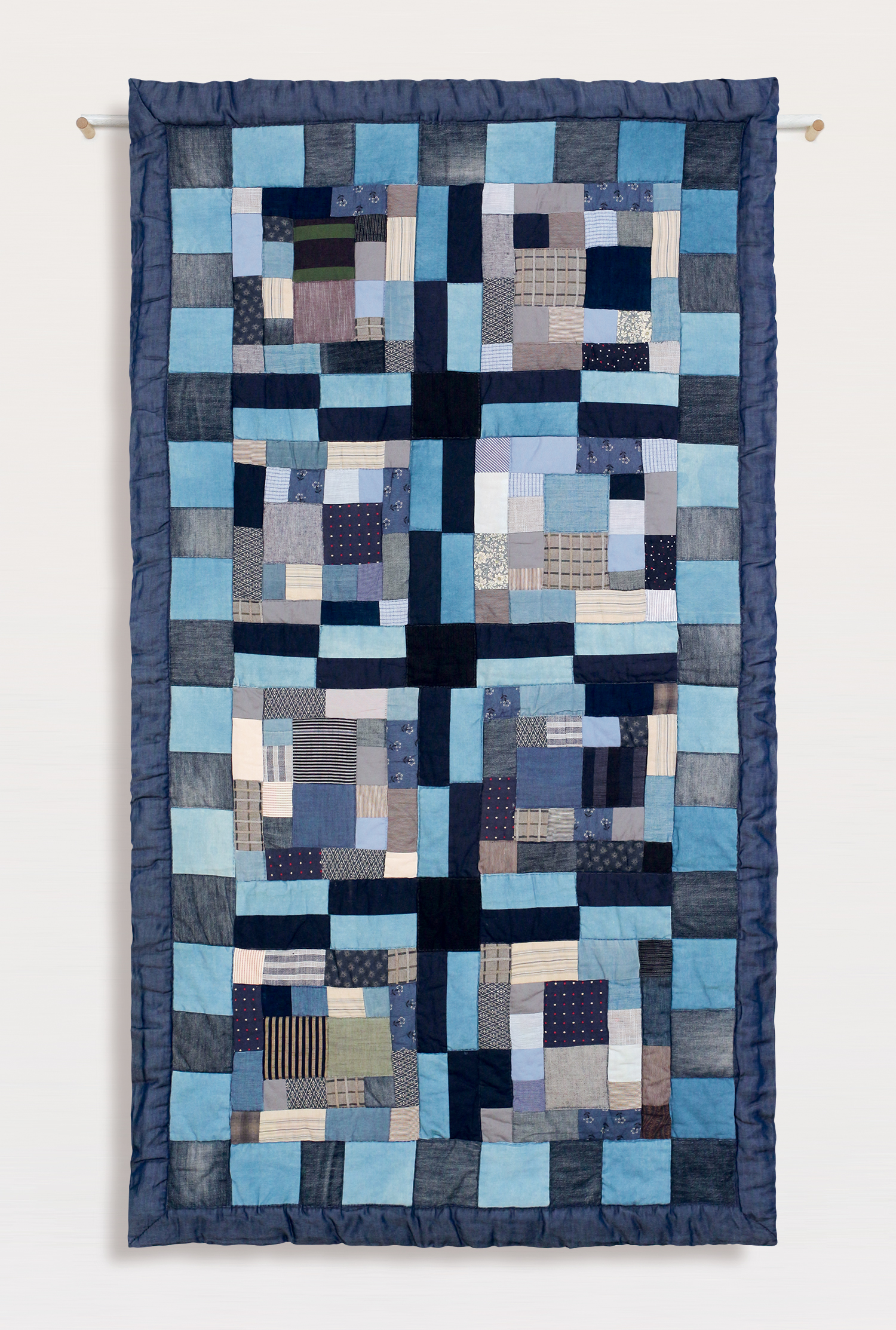 Hanging patchwork wall piece in blue tones on a light grey background – contemporary textile art by Pénélope Westberg